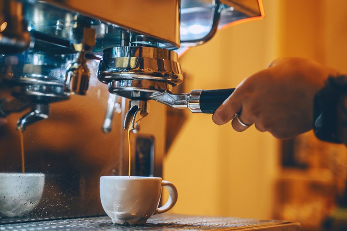 Professional coffee brewing in coffee shop. Close-up photo of espresso pouring from coffee machine. Barista make coffee cup in warm cozy atmosphere in small cafe.